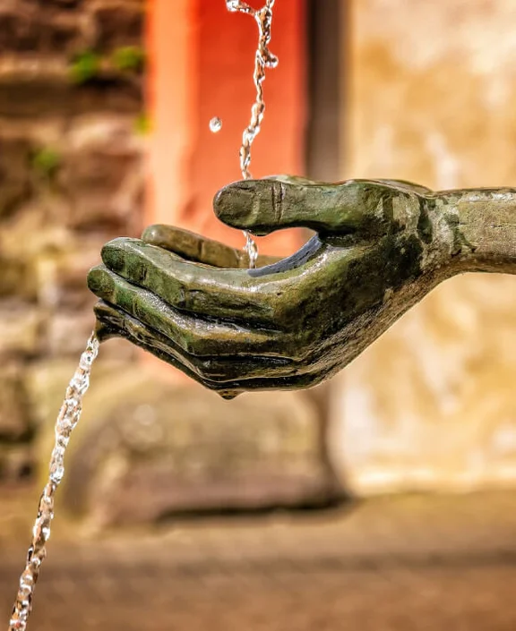 Ein Bild von einer Hand einer Steinstatue, es läuft wasser auf die Hand der Statue hinunter