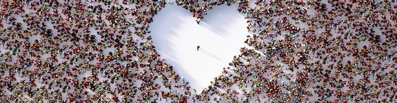 Ein Bild von sehr vielen Menschen die stehen aus der Vogelperspektive, die so stehen das eine fläche freisteht und ein Herz bildet, in der mitte des Herzes steht nur 1 Mensch
